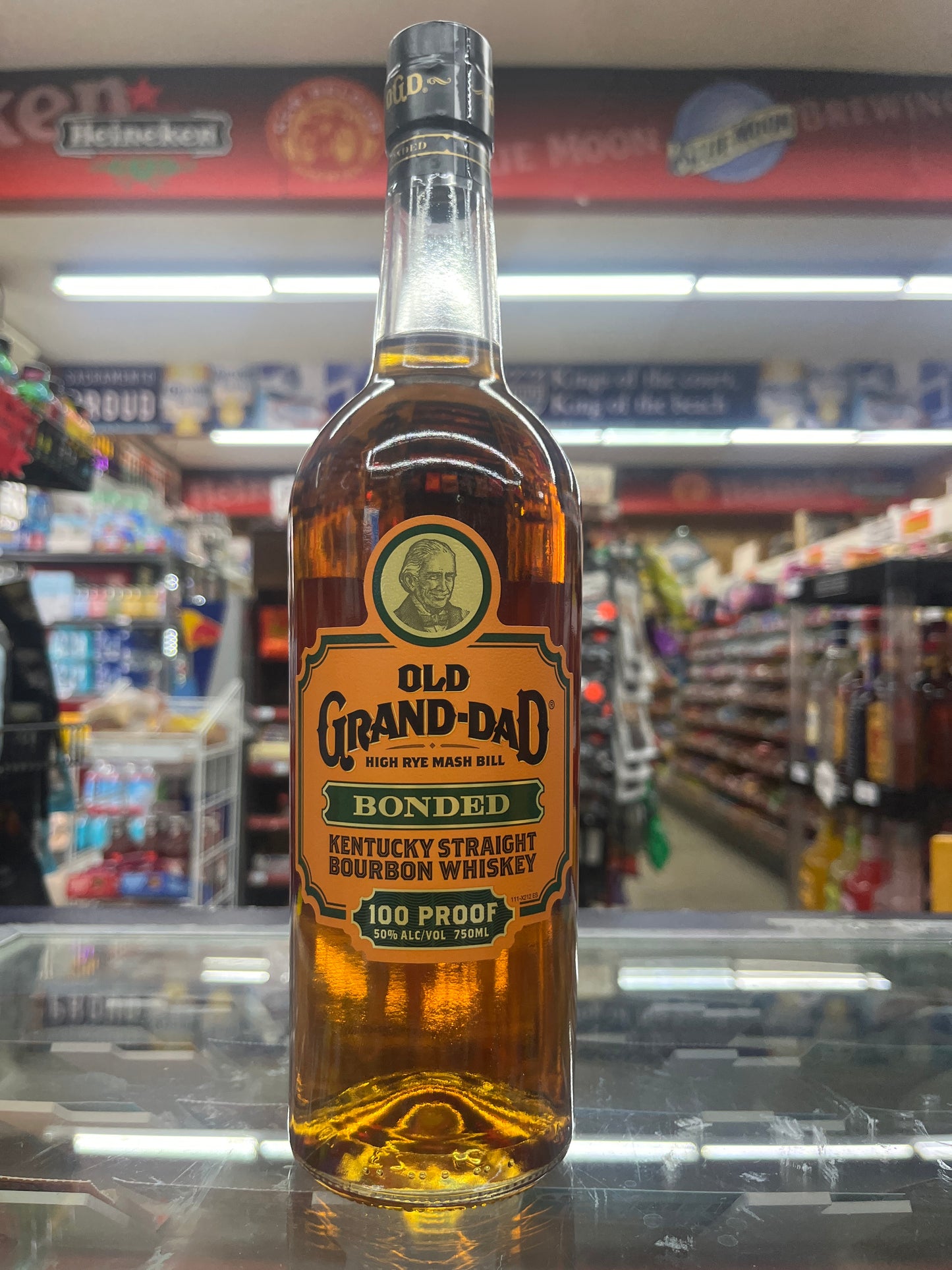 A bottle of Old Grand Dad Bonded Bourbon 750ml displayed on a shelf, with a clear label and golden colored liquid visible.