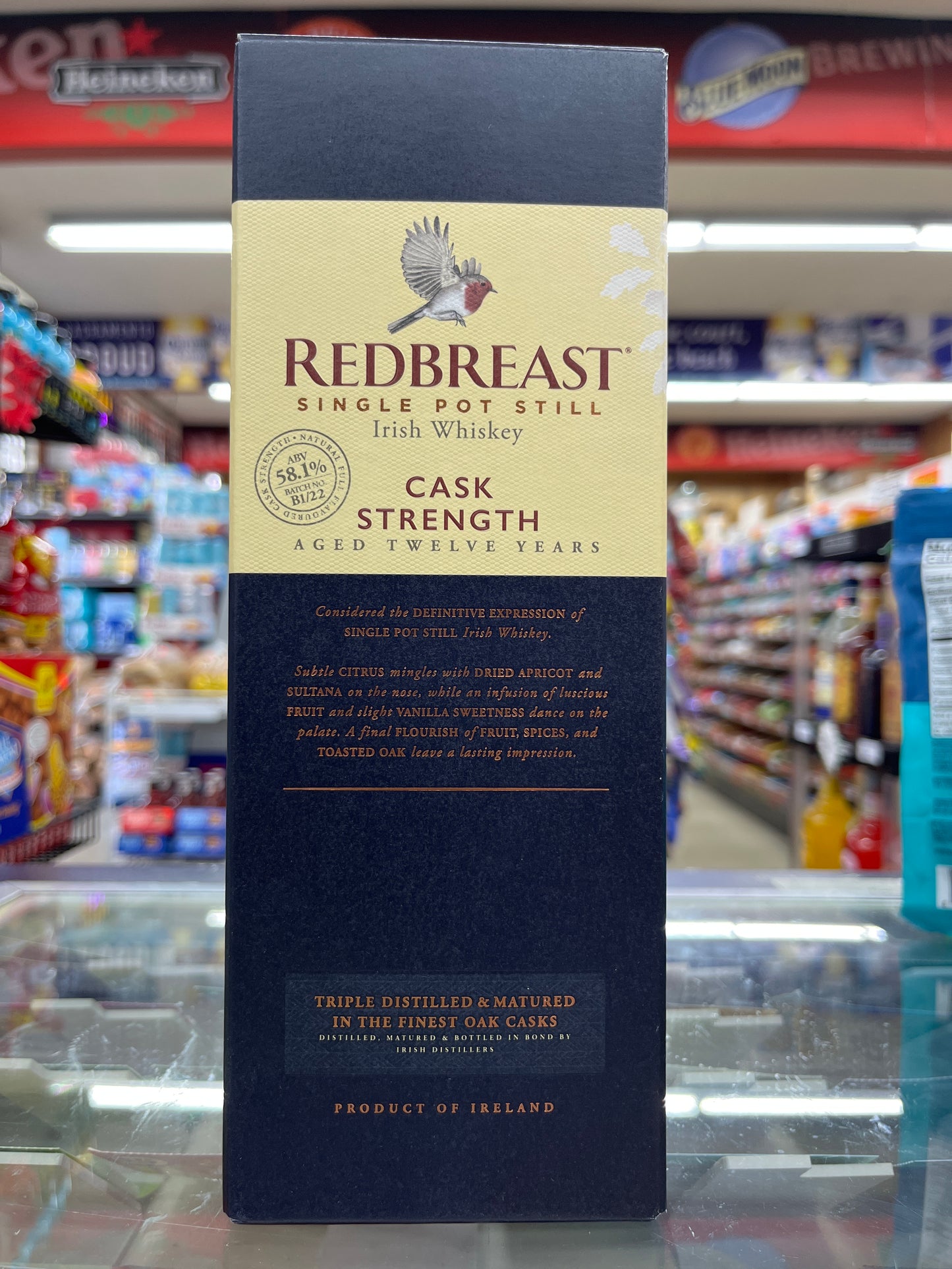 A bottle of Redbreast Irish Whiskey Cask Strength 12 yrs with a black and gold label, displayed on a store shelf.