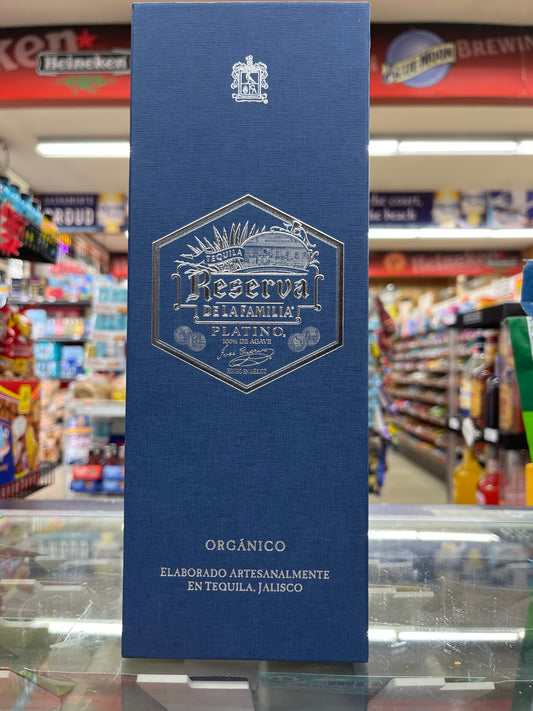 A bottle of Jose Cuervo Reserva De la Familia Platino Organic Tequila 750ml displayed on a glass shelf in a store. The packaging is predominantly blue with gold and white text and details.