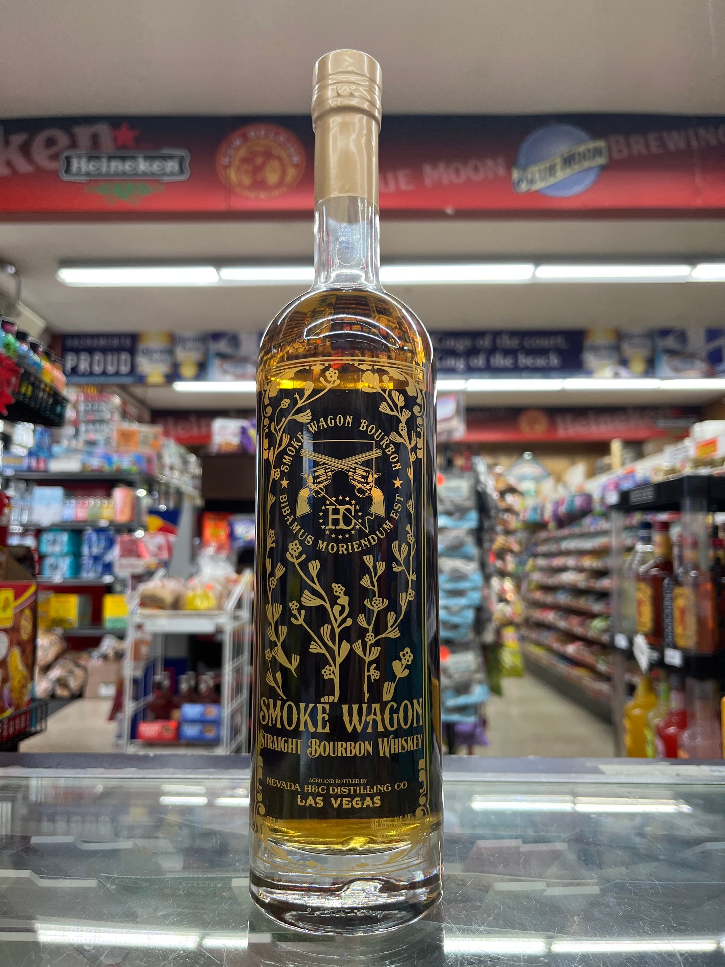 A bottle of Smoke Wagon Straight Bourbon Whiskey with a label that features gold and black text and graphics on a clear bottle, displayed on a shelf in a store.