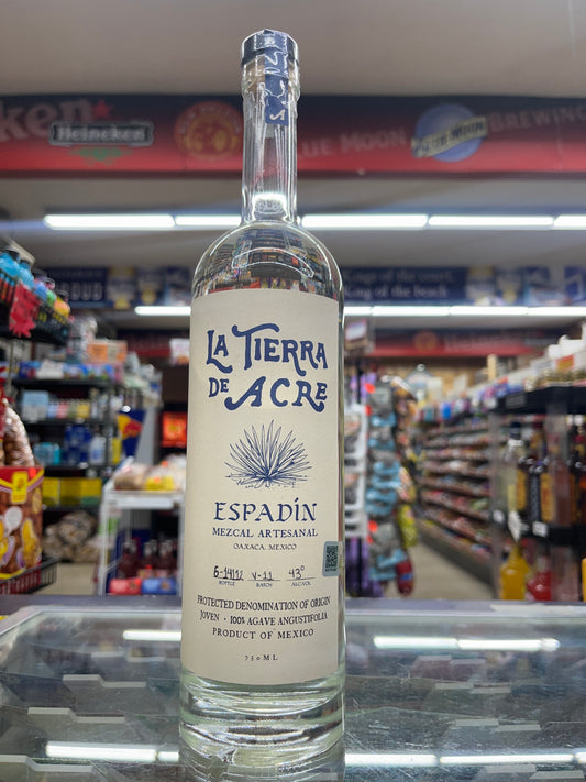A bottle of La Tierra de Acre Mezcal Espadin standing on a shelf with a blurred background.