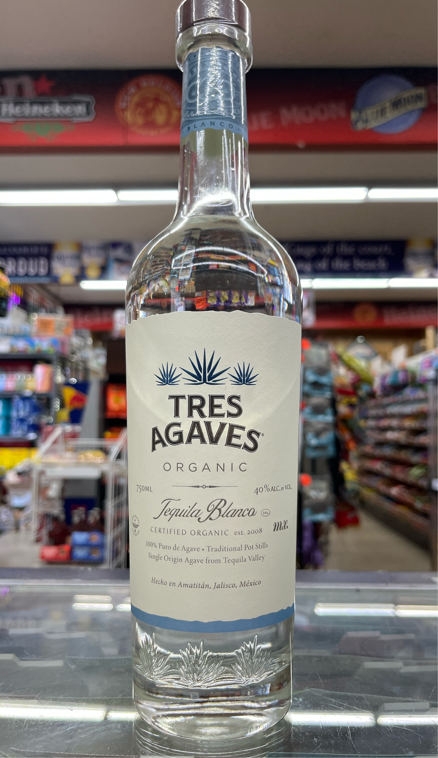 A bottle of Tres Agaves Organic Tequila Blanco with a label showcasing the brand and product name, placed on a shelf in a store.