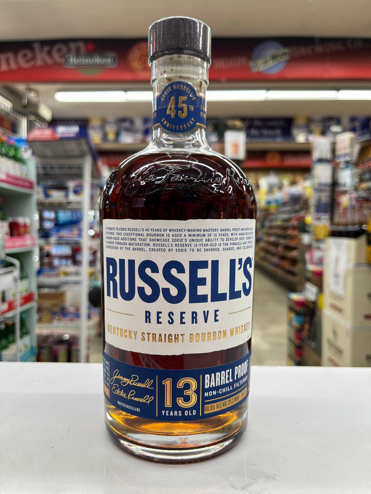 A bottle of Russell's Reserve 13 Years Old Kentucky Straight Bourbon Whiskey, 750ml, standing on a white counter inside a liquor store.
