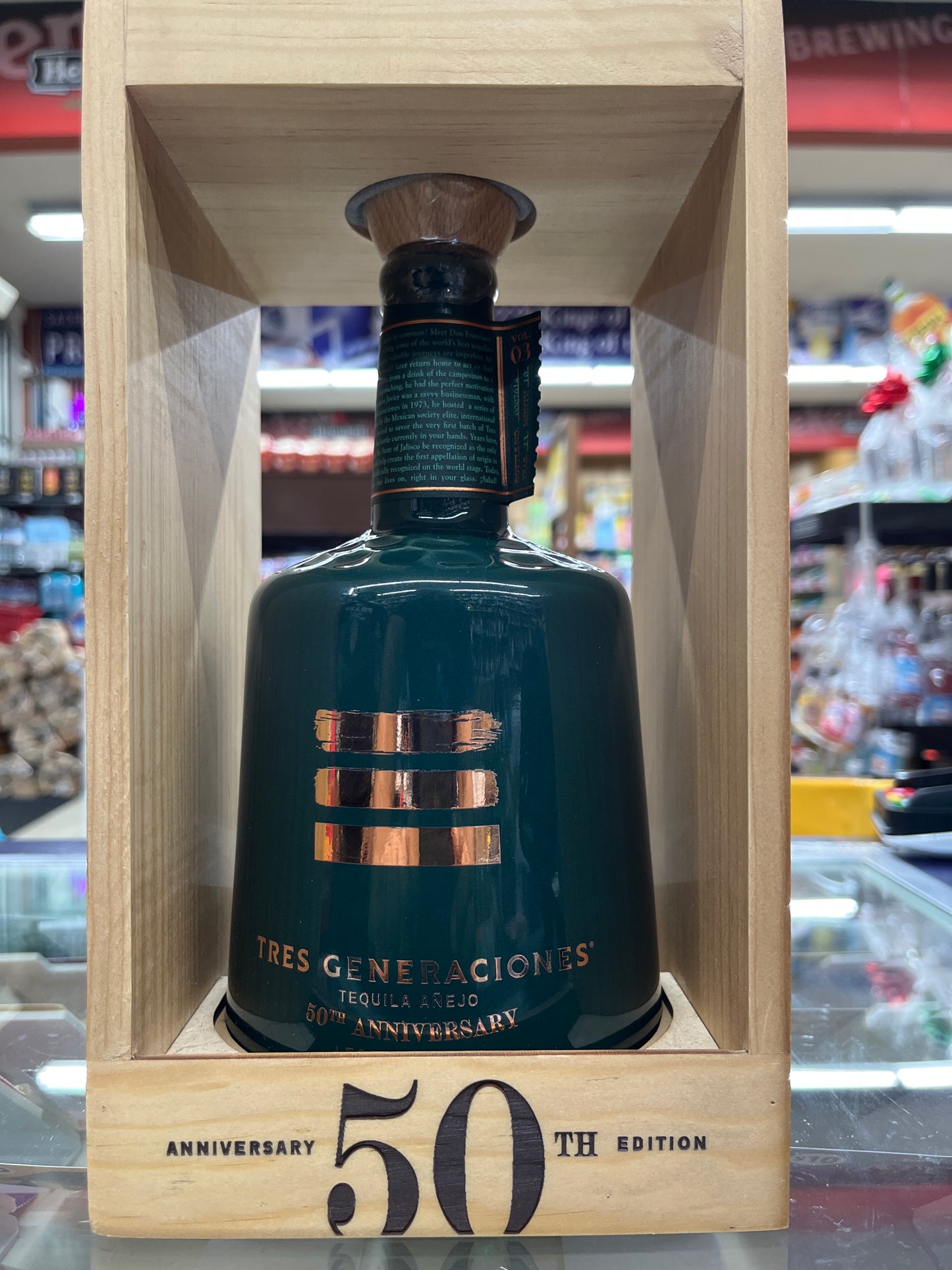 Bottle of Tres Generaciones anejo tequila in a wooden box with '50th Anniversary' text, blurred bar background