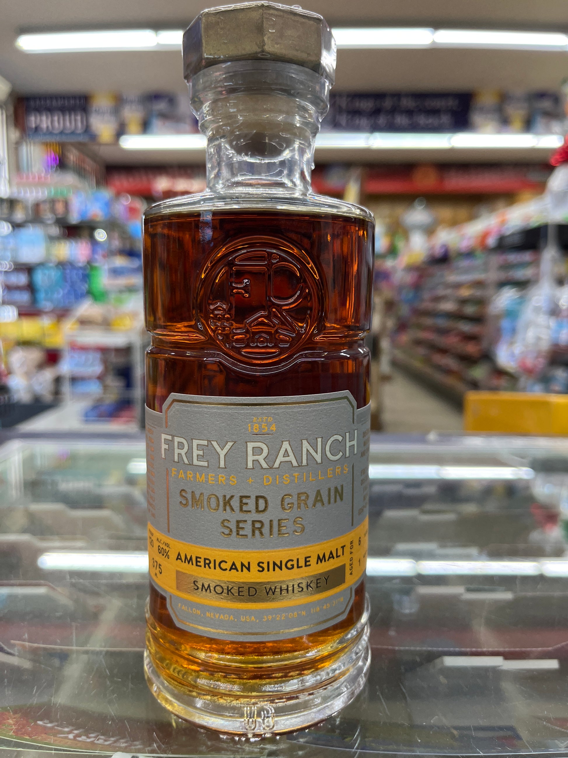 Bottle of Frey Ranch Smoked Grain Series American Single Malt Whiskey Batch 2 on a glass surface with a blurred store background.