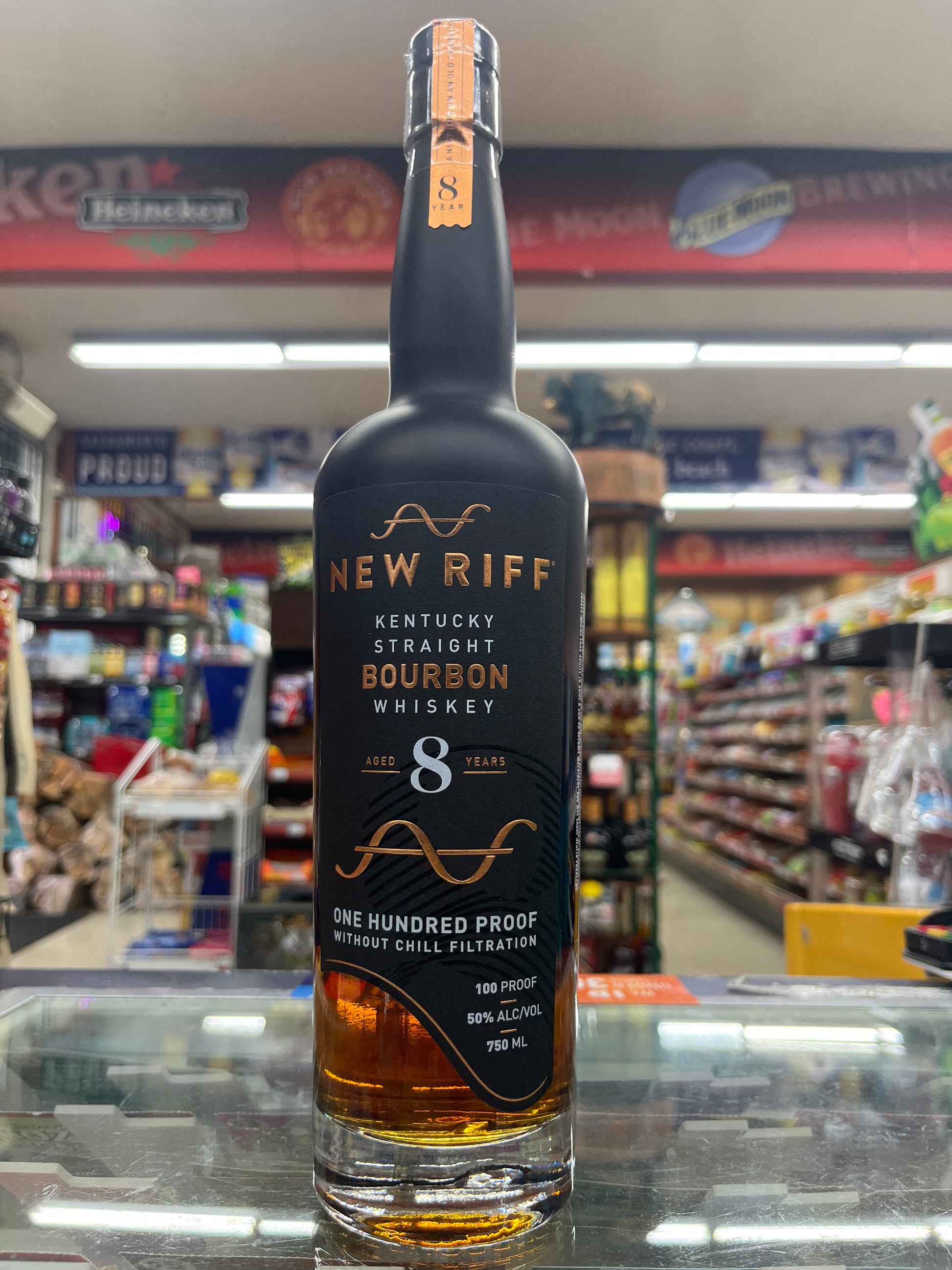 Bottle of New Riff bourbon 8 years old whiskey on a reflective surface with a blurred store background