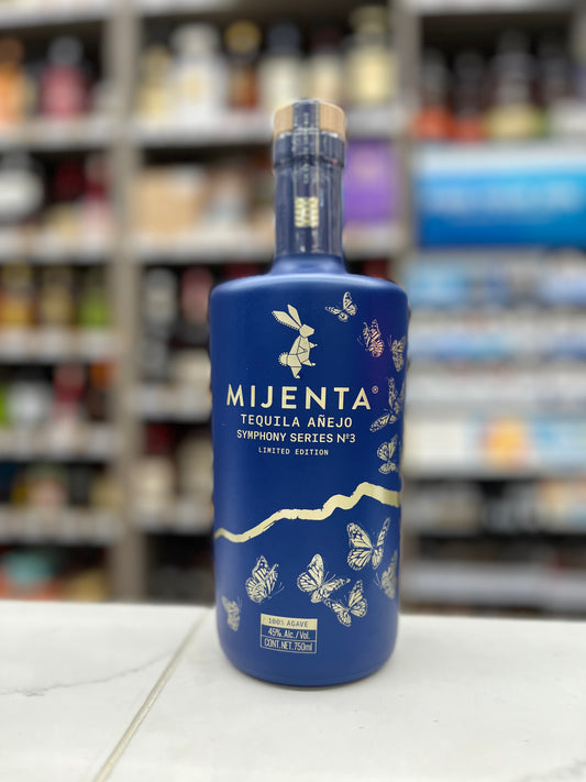 A bottle of Mijenta Tequila Anejo Symphony  No.3 Limited Edition on a white countertop with a blurred liquor store background.