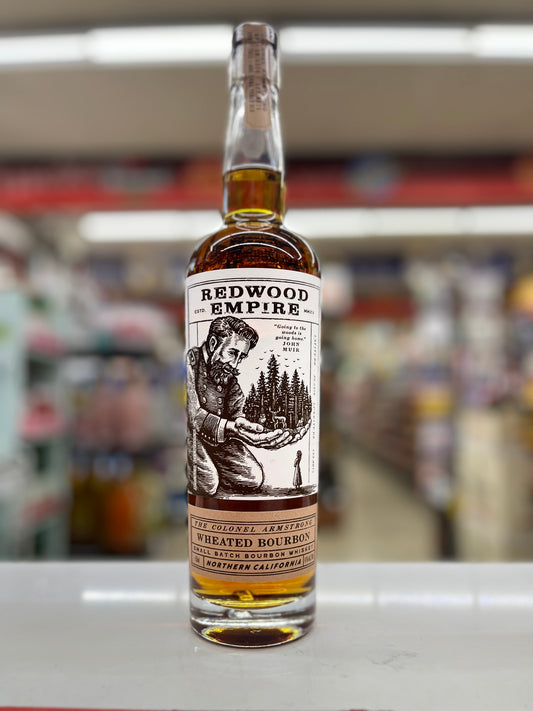 A bottle of Redwood Empire wheated Bourbon Whiskey called The colonel armstrong on a white shelf, with a blurred store background.