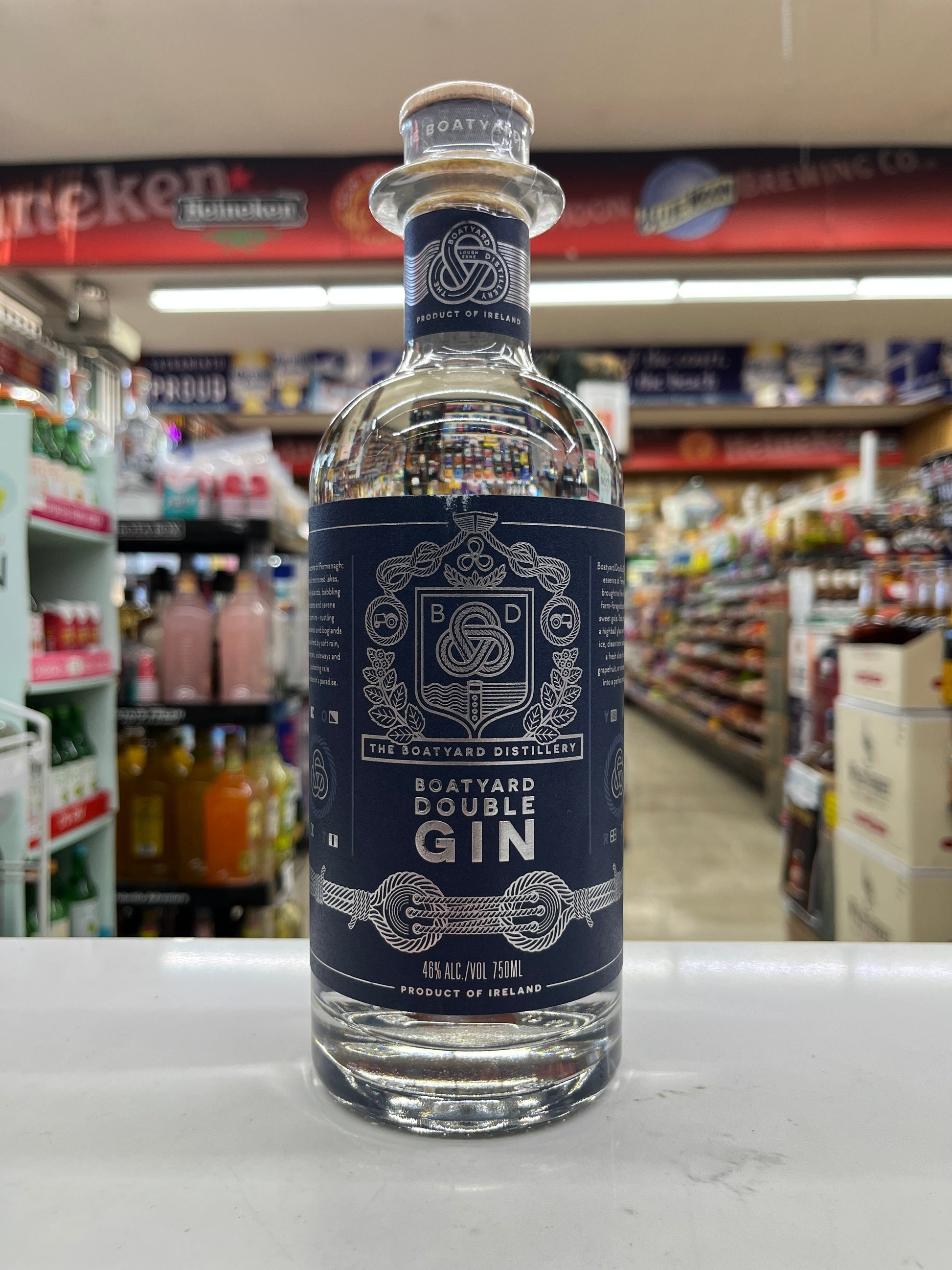 A bottle of The Boatyard Double Gin Irish Spirit distillery product, featuring a dark navy blue label with white text and crest, set on a white counter inside a retail store.