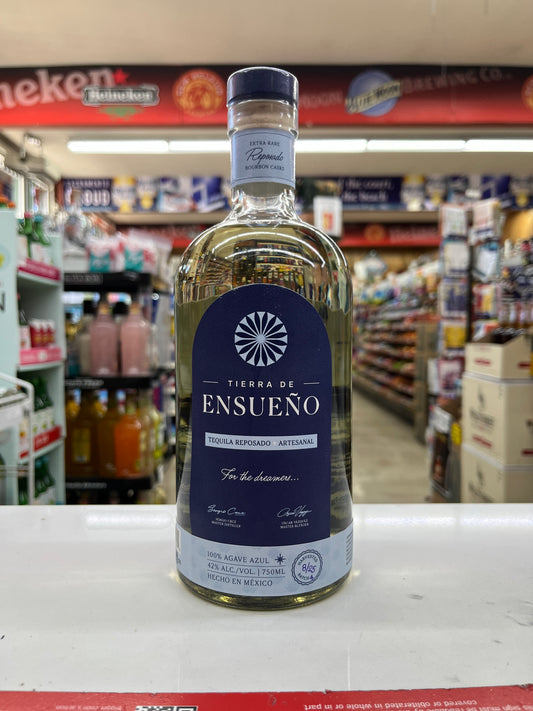 A bottle of Tierra de Ensueno Tequila Reposado Artisanal standing on a white counter inside a liquor store, with blurred shelves and products in the background.