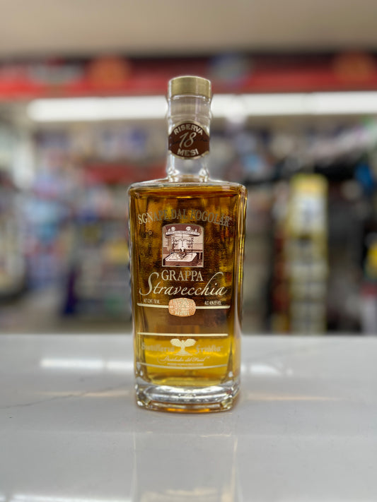 Bottle of Grappa Stravecchia aged 18 months sitting on a white shelf with blurred background