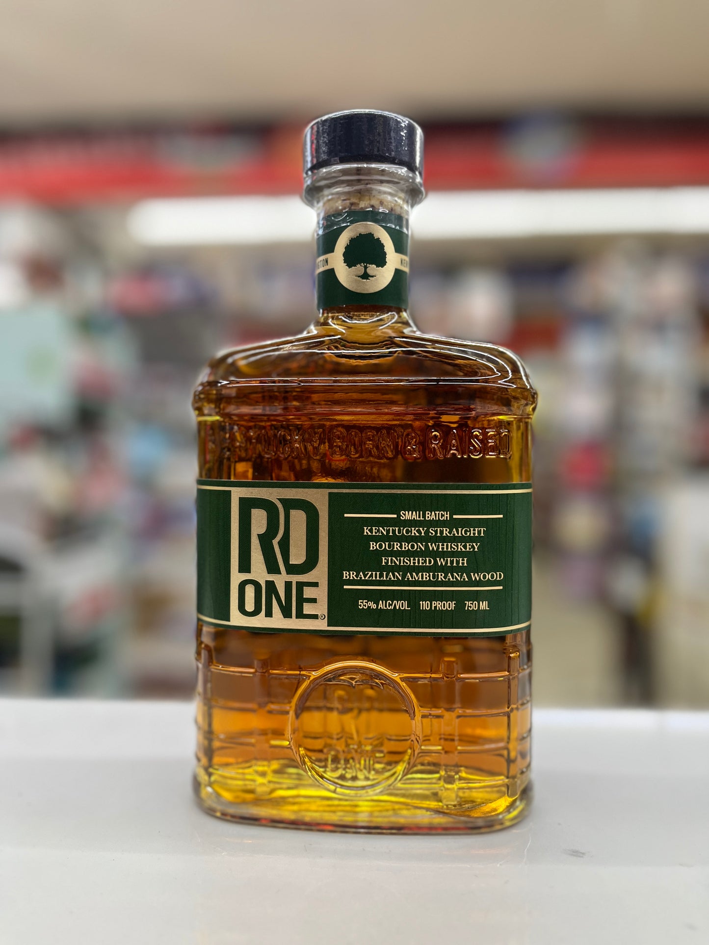 A bottle of RD One Kentucky Straight Bourbon Whiskey with Brazilian Amurana Wood finish, displayed on a white surface with a blurred background.