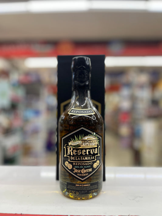 A bottle of Reposado Reserva Delafamila Jose Guerroro tequila standing upright in front of its black packaging box on a white counter, with a blurred store background.