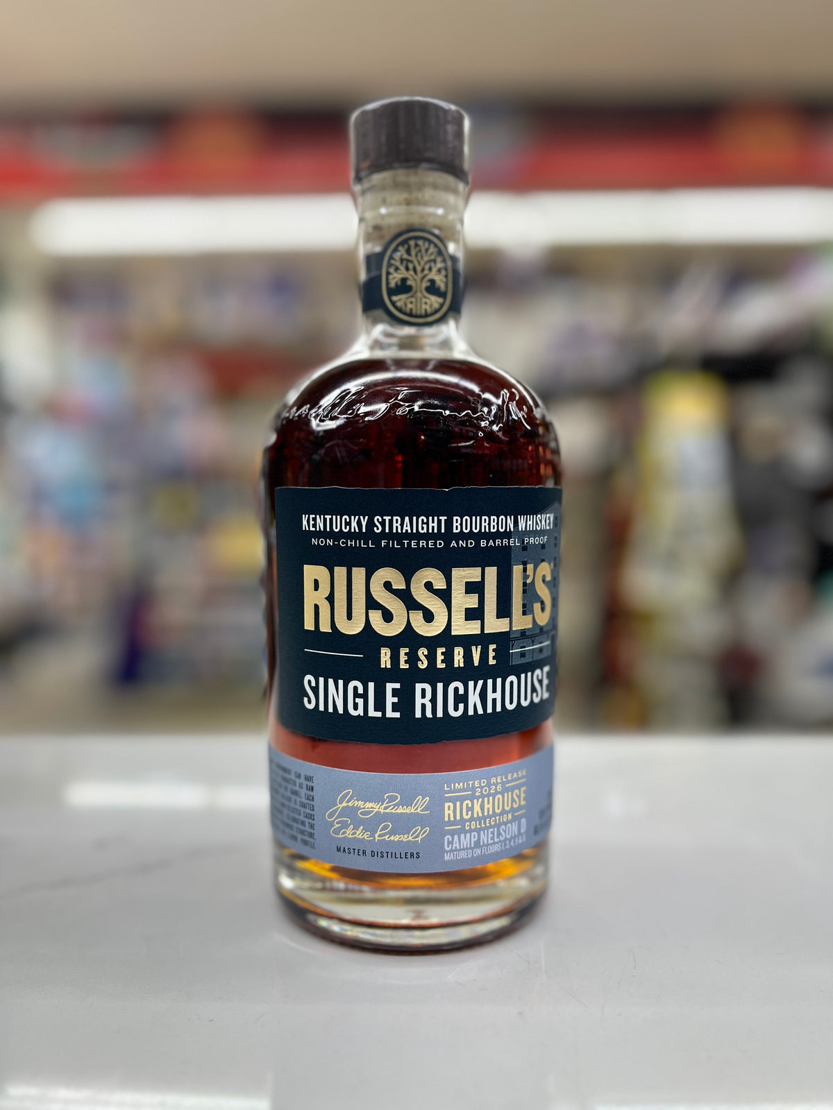 A bottle of Russell's Reserve Single Rickhouse Kentucky Straight Bourbon Whiskey, showing the amber liquid and dark blue label, set against a blurred store background.