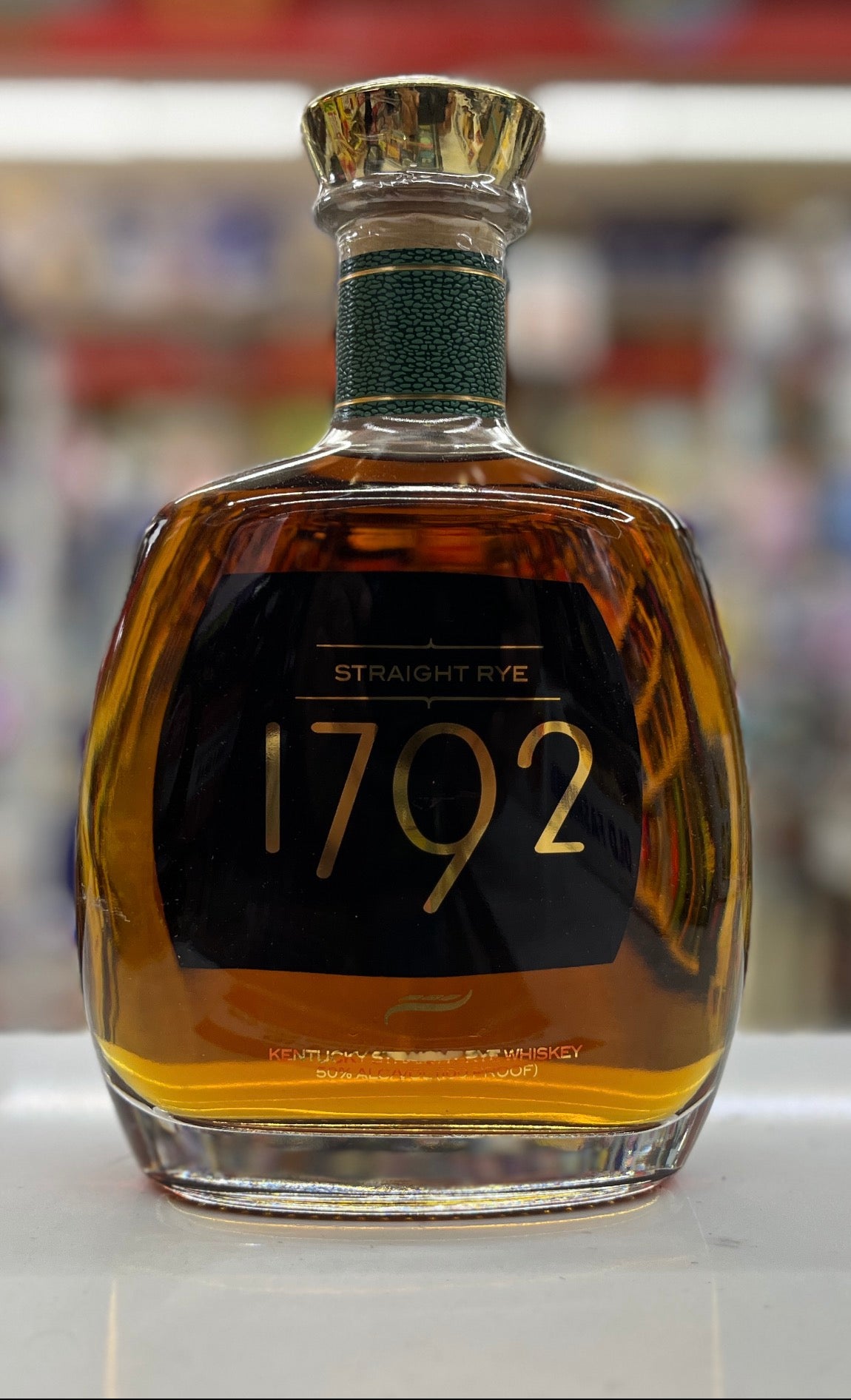 A bottle of 1792 Straight Rye whiskey with amber liquid, a black label with gold lettering, and a gold cap, set against a blurred background.