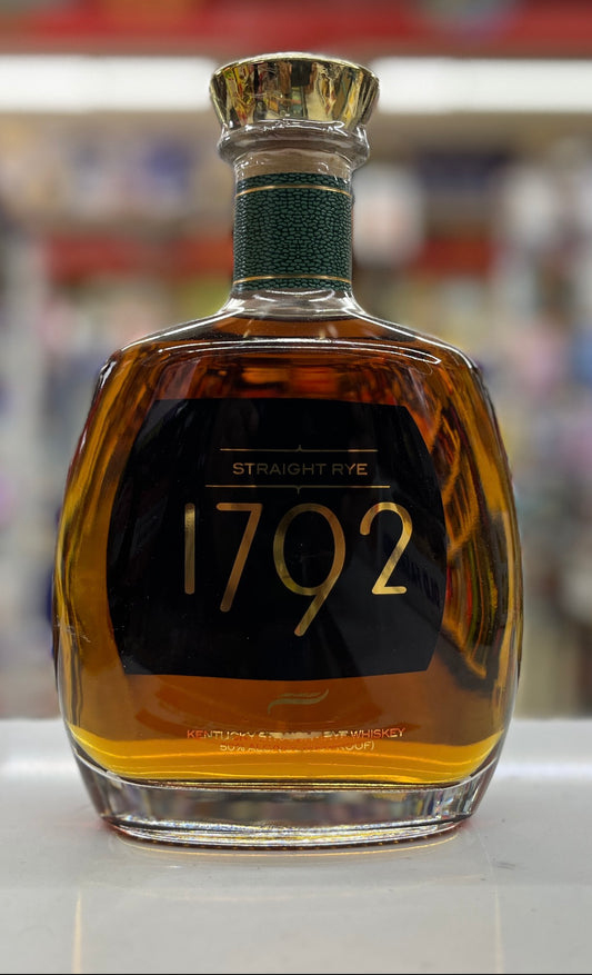 A bottle of 1792 Straight Rye whiskey with amber liquid, a black label with gold lettering, and a gold cap, set against a blurred background.