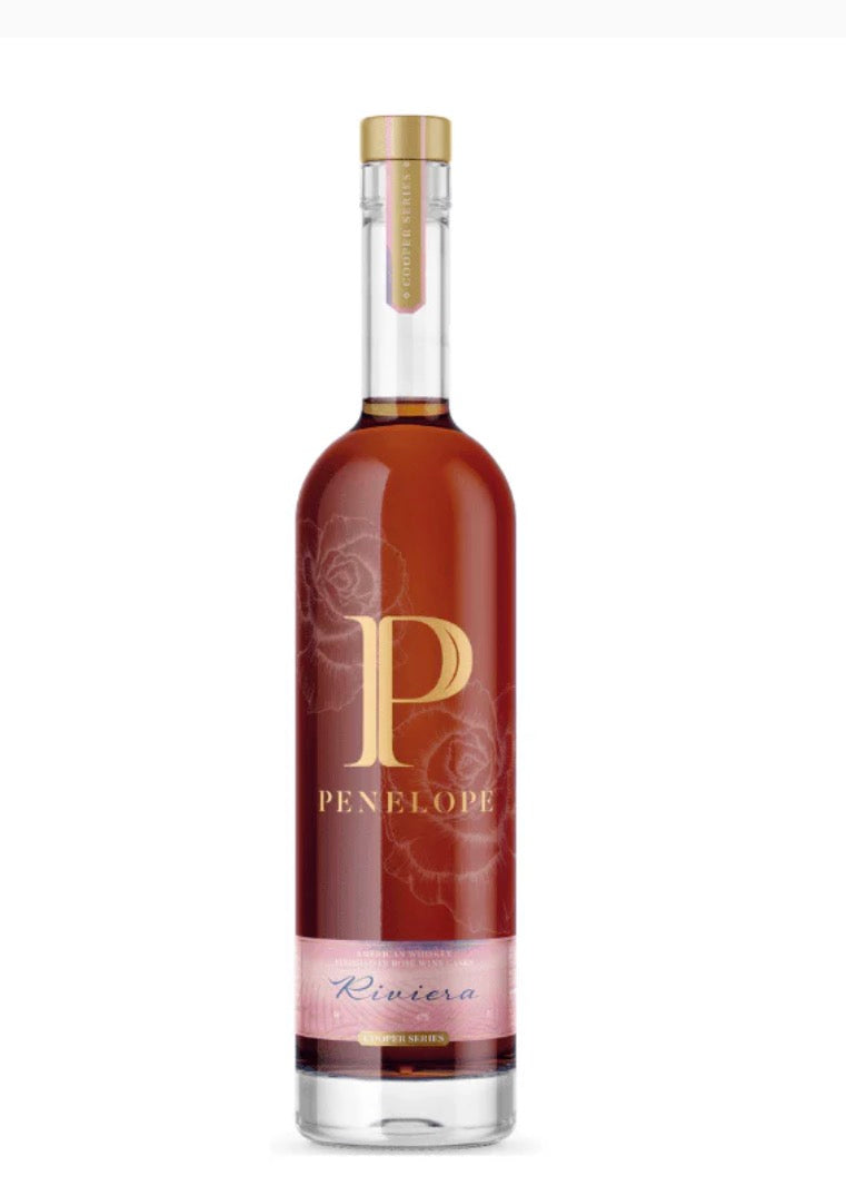 A bottle of Penelope Riviera Whiskey with a dark amber-brown liquid, featuring a gold 'P' logo and 'PENELOPE' brand name on the label, and a pink band near the bottom.