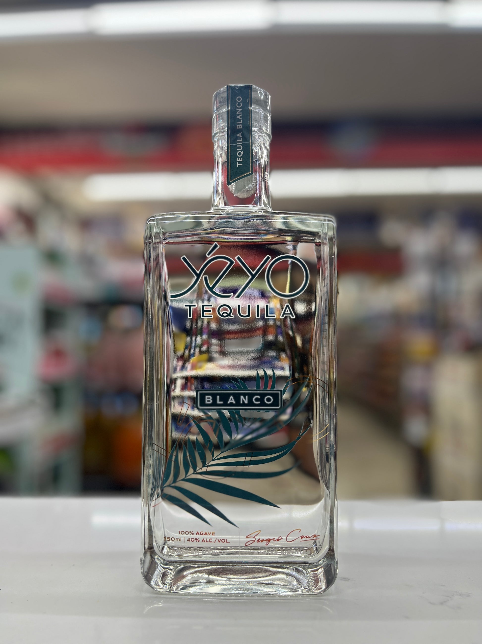 A bottle of Yeyo Tequila Blanco standing on a white surface with a blurred store background.