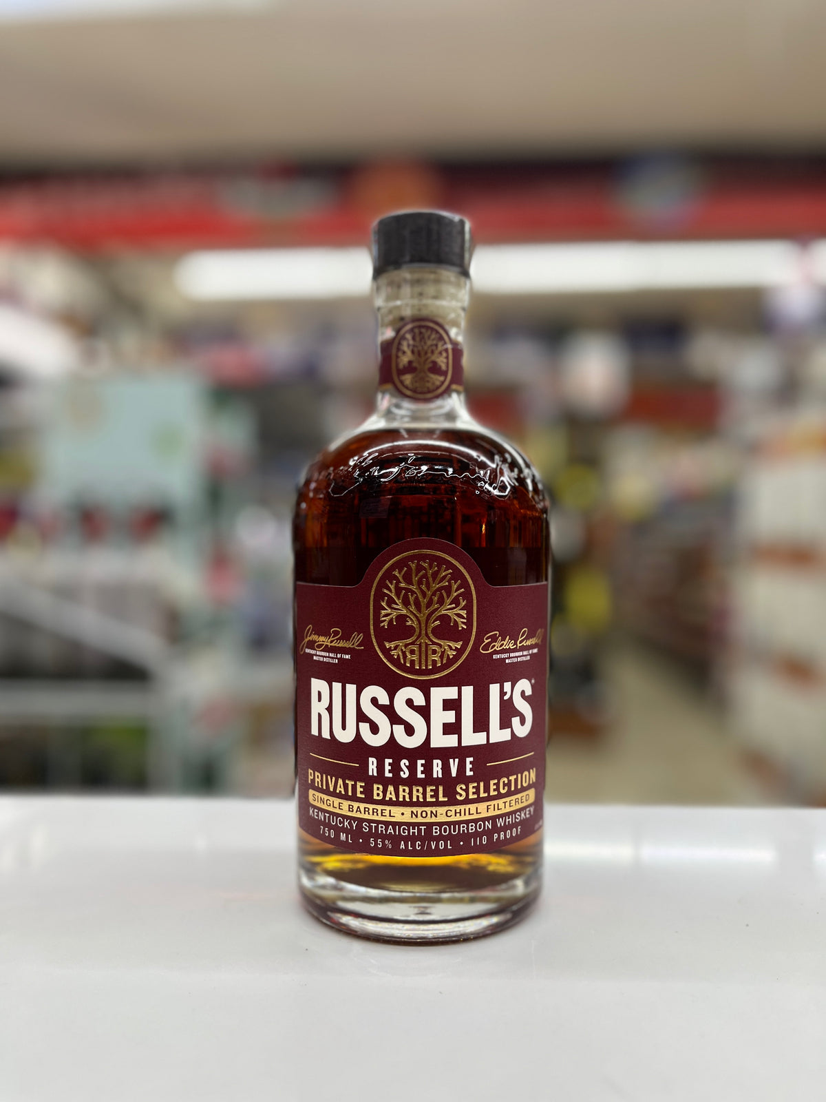 A bottle of Russell's Reserve Kentucky Straight Bourbon Single Barrel Whiskey sits on a white counter in a blurred retail store environment.