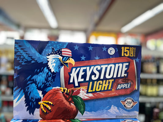 A box of Keystone Light Apple 15-pack beverage packaging displayed on a store shelf, featuring a blue eagle with an American flag hat and a red apple graphic.