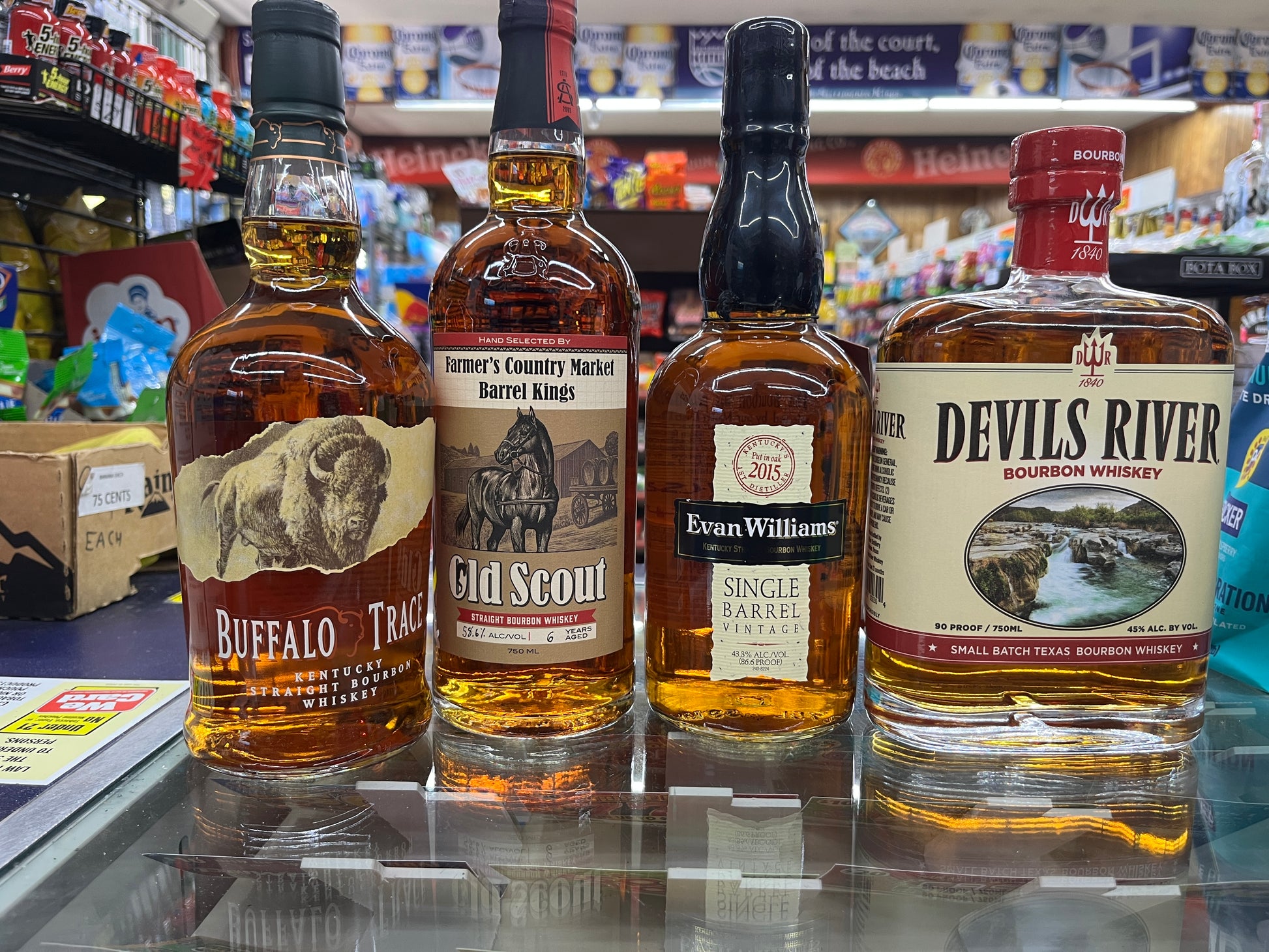 Four bottles of whiskey on a store shelf with various products in the background